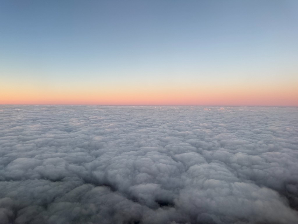 Soft cloud tops beneath a pink and blue horizon seen from an airplane