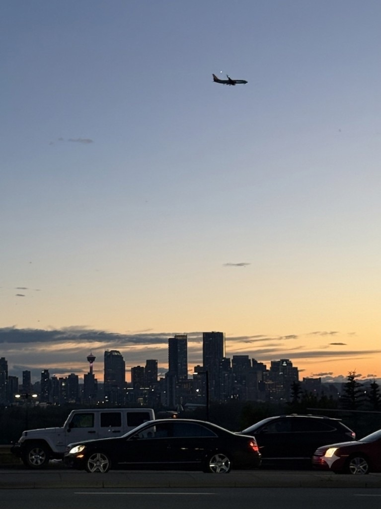 Calgary skyline at dusk with an airplane crossing the sky