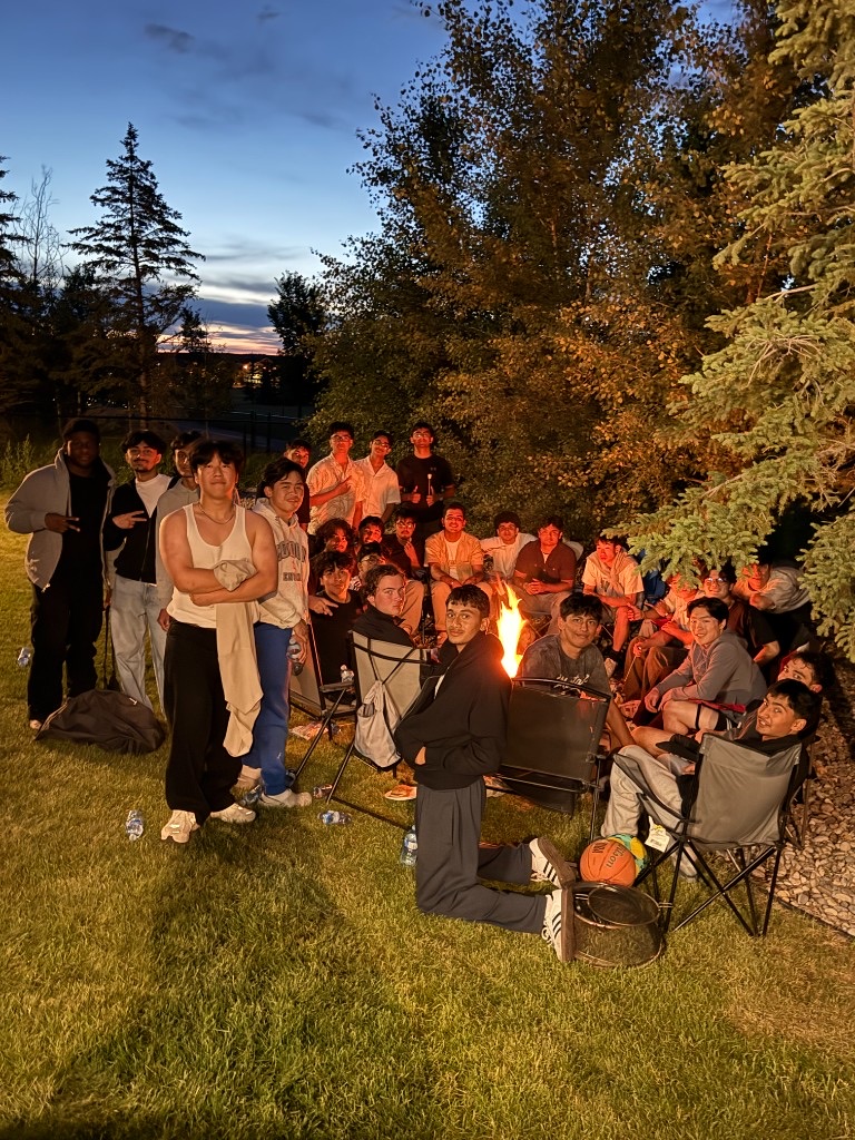 A large group of friends gathered around a backyard fire at sunset