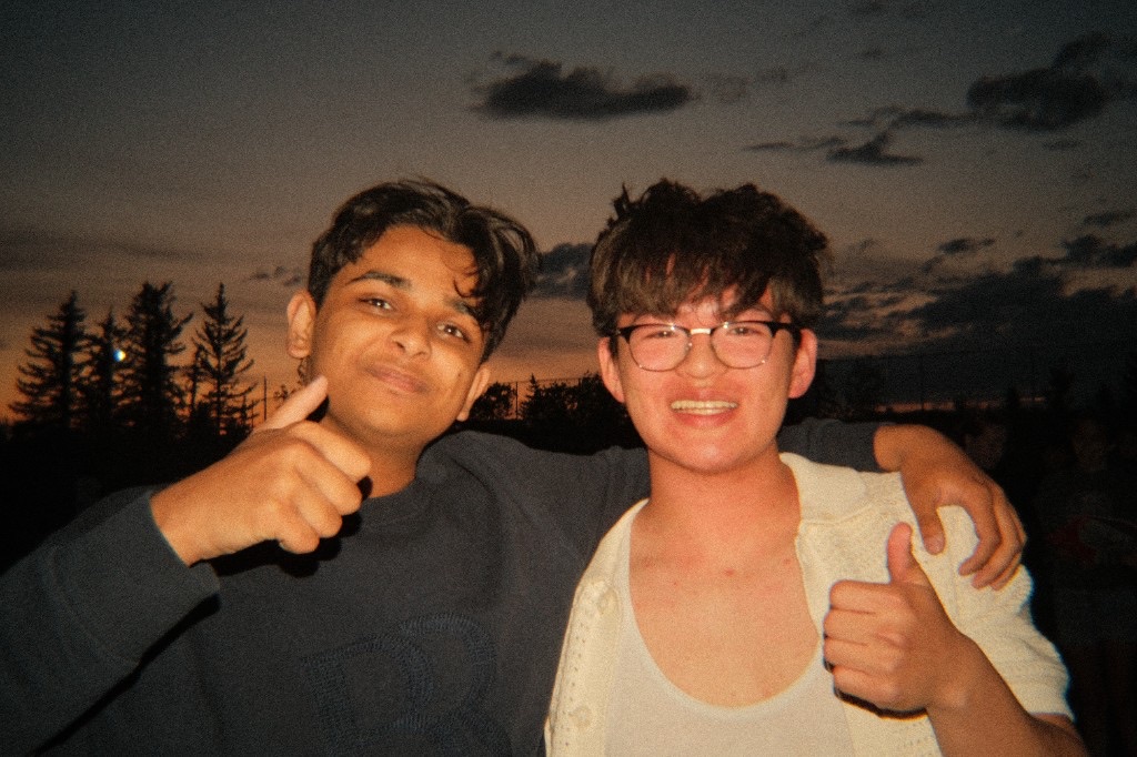 Ali and a friend posing together with thumbs up at dusk