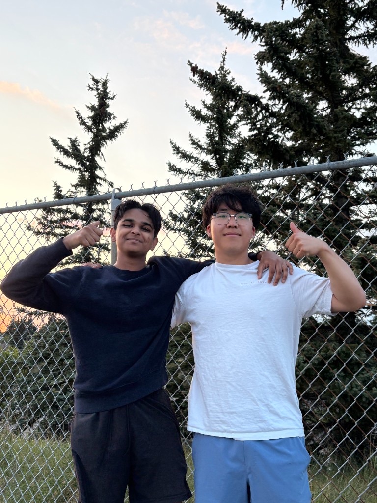 Ali and a friend standing with their arms around each other by a fence at sunset