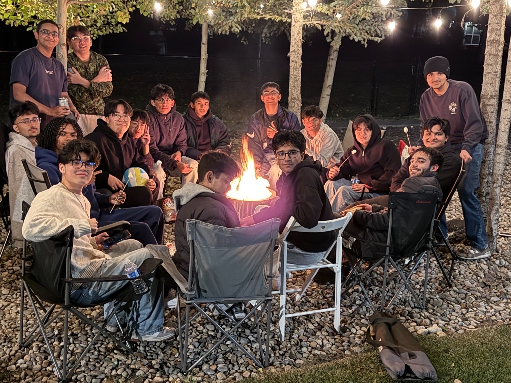 Friends sitting together around a backyard fire under string lights