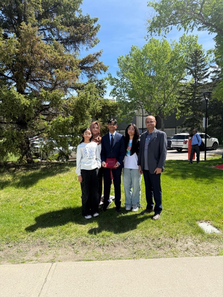 Ali in a suit holding his diploma with family on graduation day