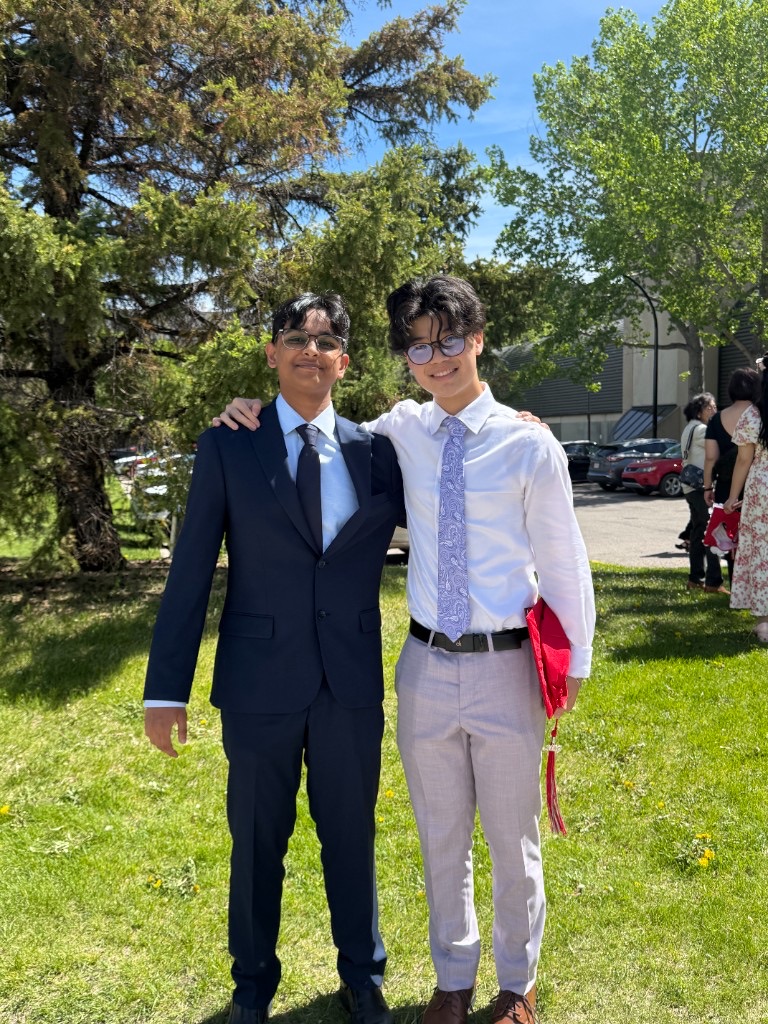 Ali in a navy suit standing with a friend outdoors on graduation day