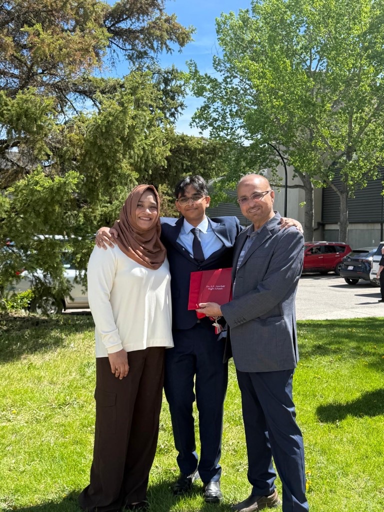 Ali in a suit celebrating graduation with his parents outdoors
