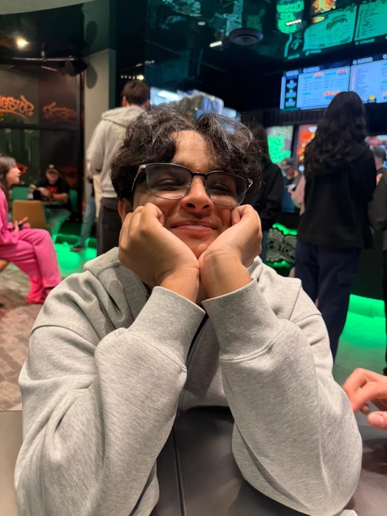 Ali smiling at a restaurant with his chin resting in his hands