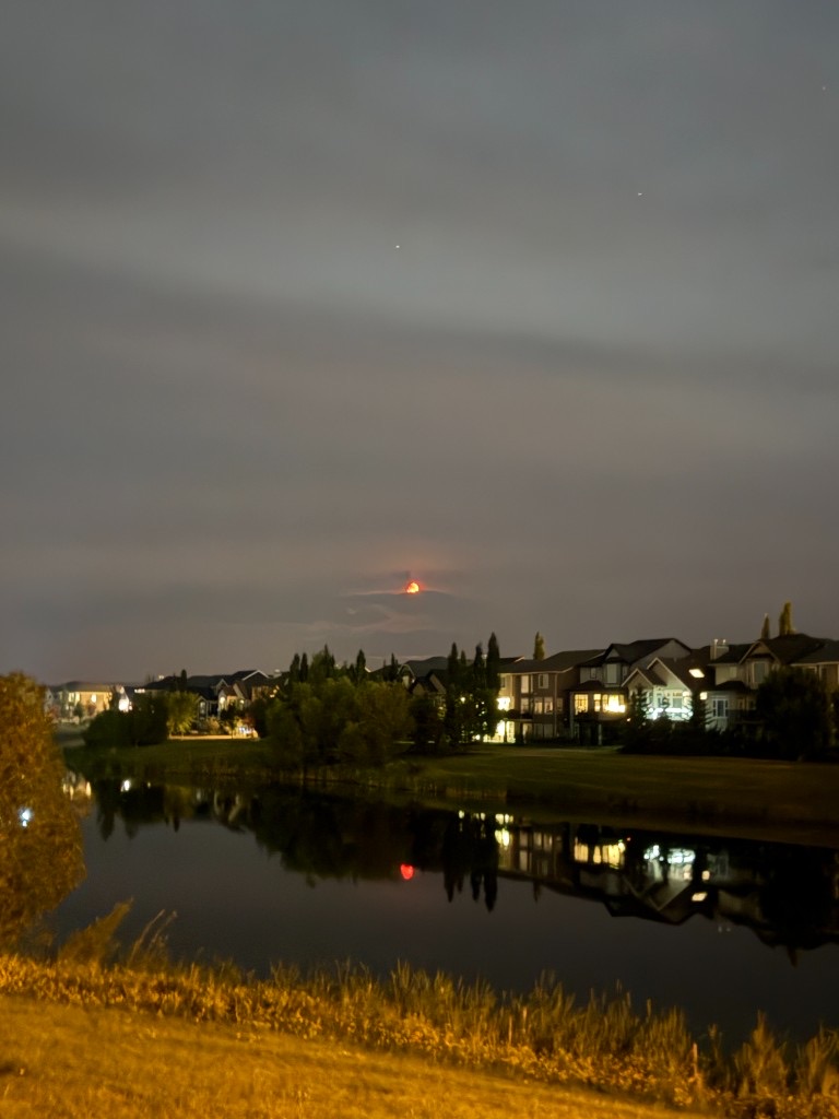 A red moon low over a quiet lake and suburban homes at night