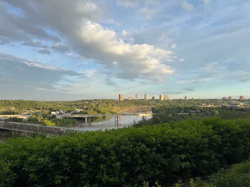A green river valley and city bridges beneath a wide summer sky